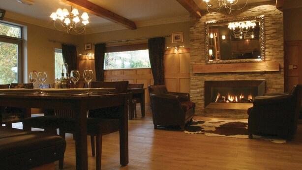 A cozy living room with a fireplace, wooden furniture, and a chandelier. - Waterloo Hotel Lodge (Betws-Y-Coed)