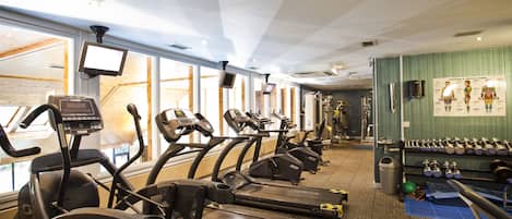 Un gimnasio con cintas de correr, bicicletas estáticas y pesas.