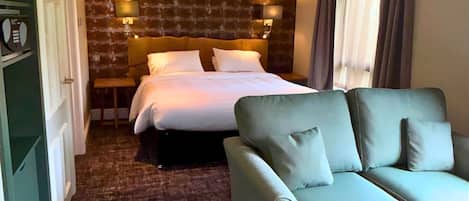 A hotel room with a bed, a sofa, a brick-patterned wall, and a window with curtains.