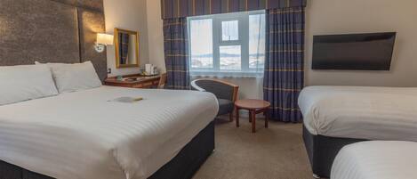 A hotel room with two beds, a desk, a chair, a TV, and a window with curtains.