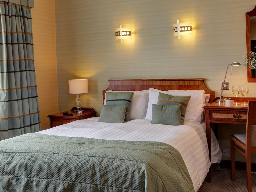 Une chambre d’hôtel avec un grand lit, des tables de chevet, un bureau et une chaise. Il y a deux lampes fixées au mur et un miroir au-dessus du bureau.