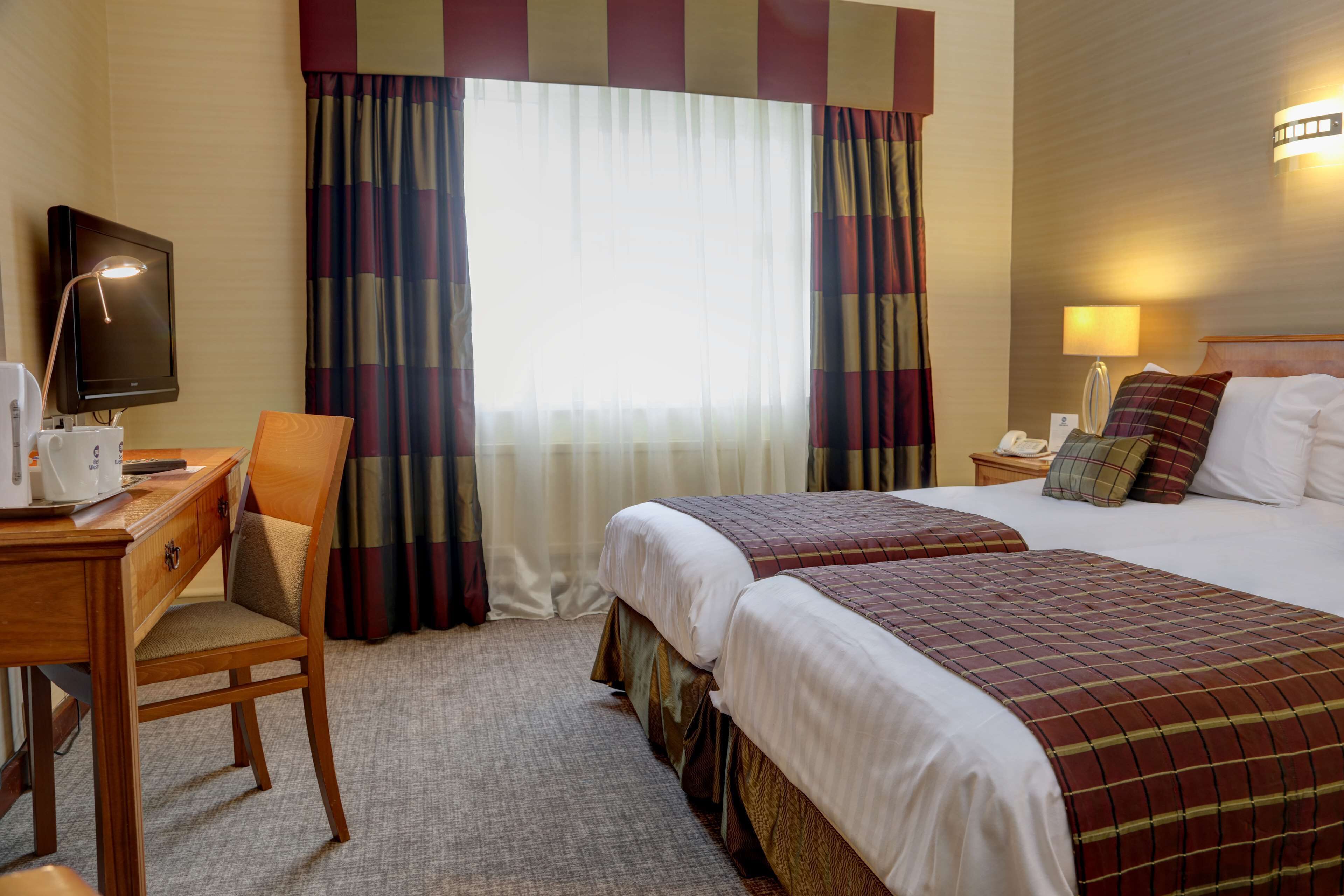 A hotel room with two beds, a desk with a lamp, a chair, and a television.