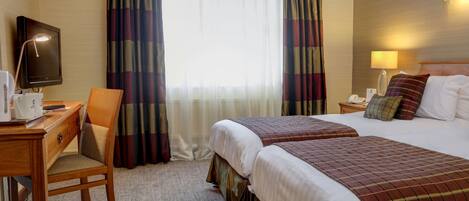 Habitación de hotel con dos camas, un escritorio con lámpara, una silla y un televisor.