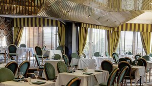 A dining area with tables set for service, green upholstered chairs, and a patterned ceiling. - Best Western Aberavon Beach Hotel (Port Talbot)