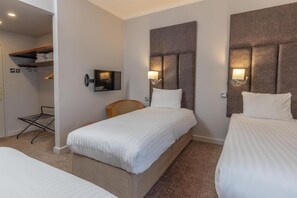 A hotel room with two beds, a TV, a headboard with a light, and a small closet with shelves.