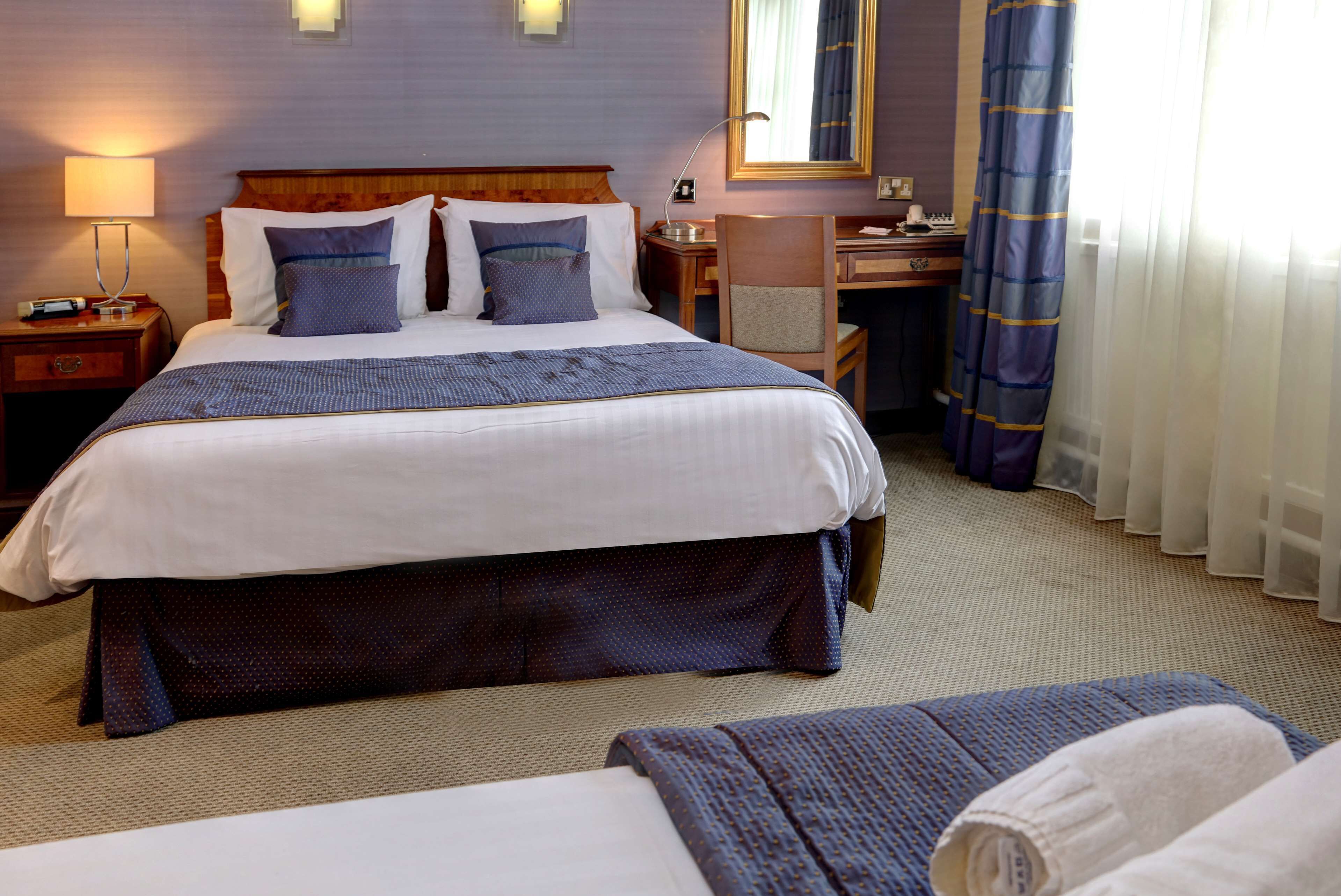 Habitación de hotel con una cama grande, un escritorio, una silla y una ventana con cortinas.