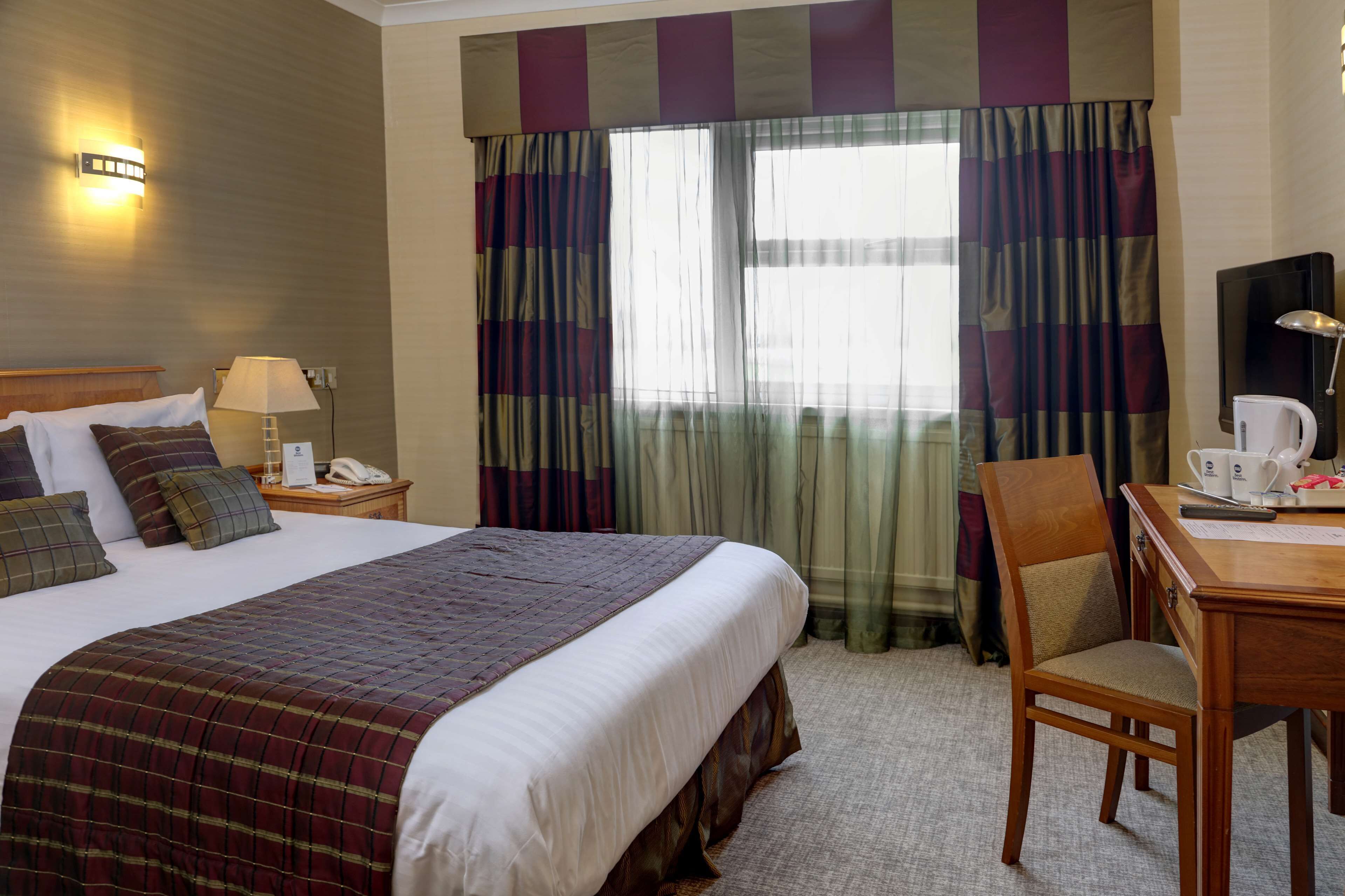 Een hotelkamer met een groot bed, een bureau met stoel, een televisie en een raam met gordijnen.