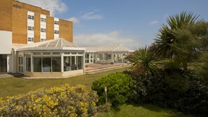 A conservatory with a glass roof, surrounded by a garden with yellow flowers and a palm tree. - Best Western Aberavon Beach Hotel (Port Talbot)