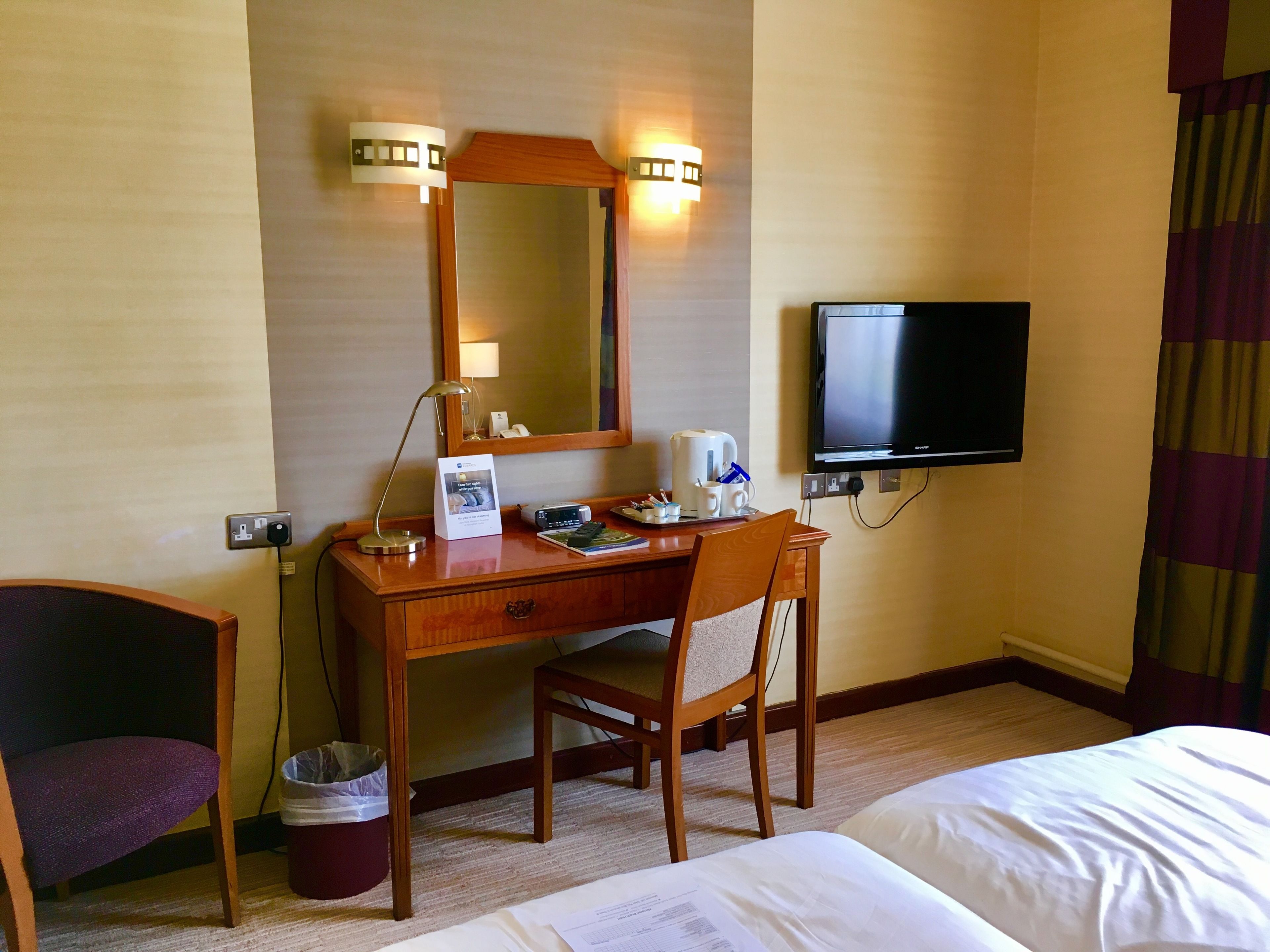 Ein Hotelzimmer mit einem Holztisch, einem Sessel, einem Bett, einem Fernseher und einem Papierkorb.