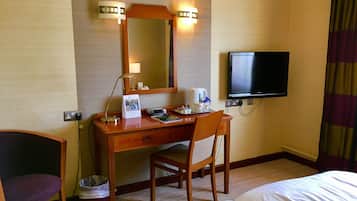 Ein Hotelzimmer mit einem Holztisch, einem Sessel, einem Bett, einem Fernseher und einem Papierkorb.