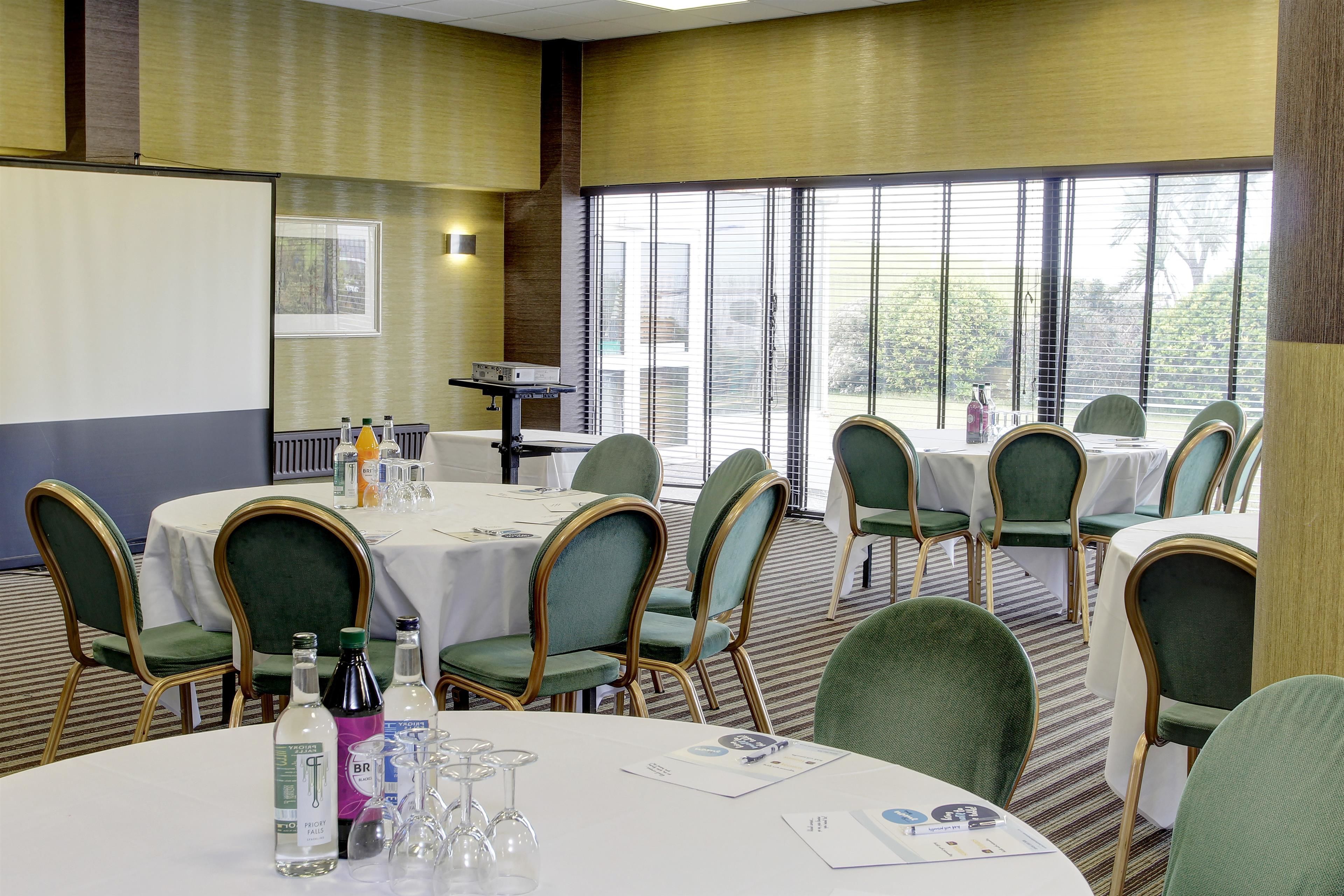 A conference room with round tables, green upholstered chairs, and a projector screen.