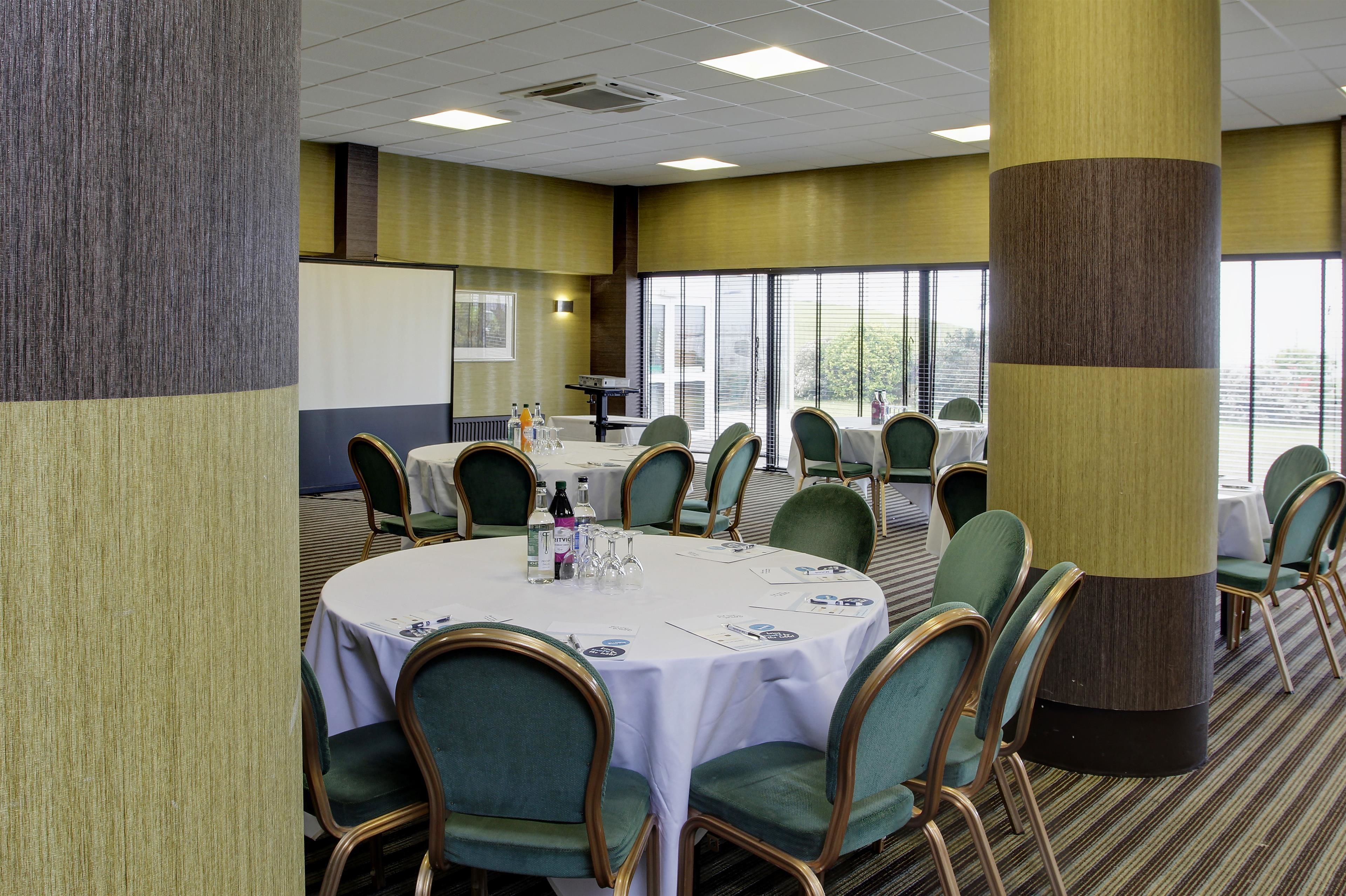 A conference room with round tables, green upholstered chairs, and a white tablecloth.