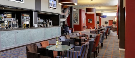 A hotel lobby with a bar, seating area, and a staircase.