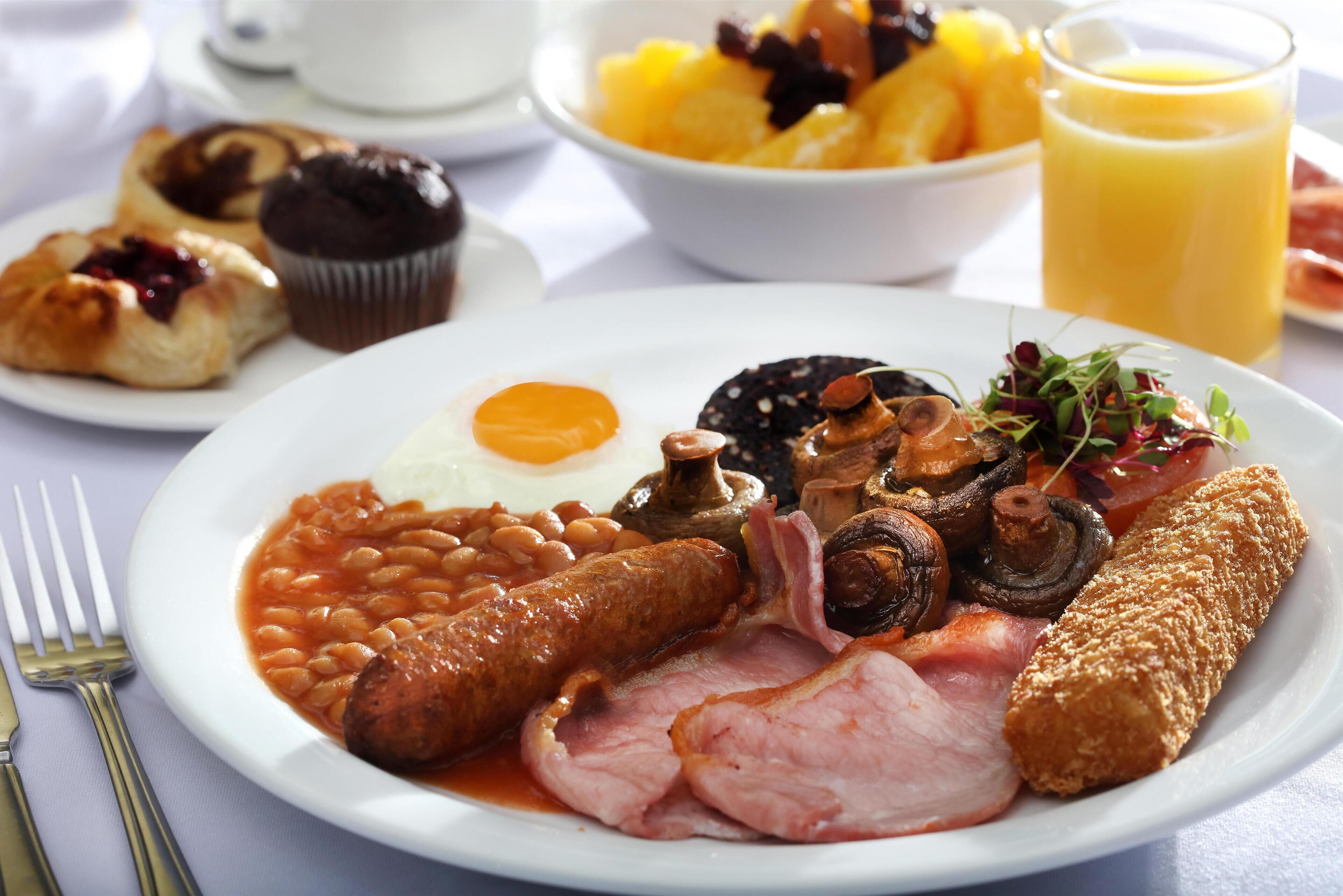 A breakfast plate with beans, sausages, ham, mushrooms, and a poached egg.