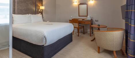 A hotel room with a large bed, a desk with a chair, a small round table, and a mirror.