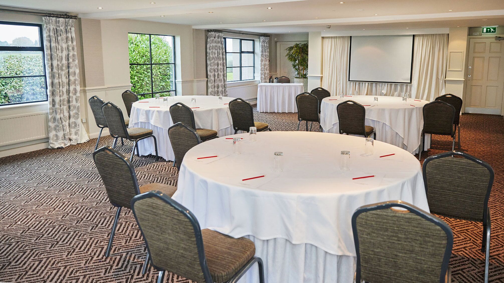 Un salón de conferencias con mesas redondas, sillas y una pantalla de proyección.