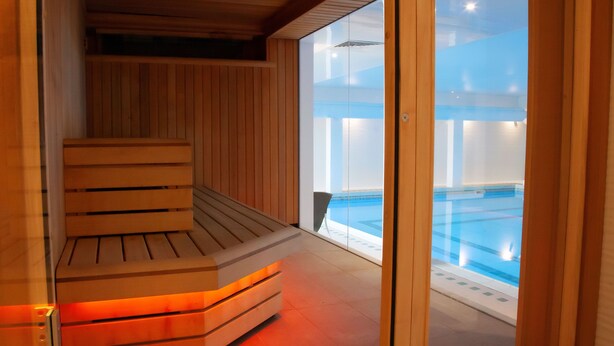 A sauna with a wooden bench and glass doors leading to a pool area. - The Wrightington Hotel & Health Club (Wigan)