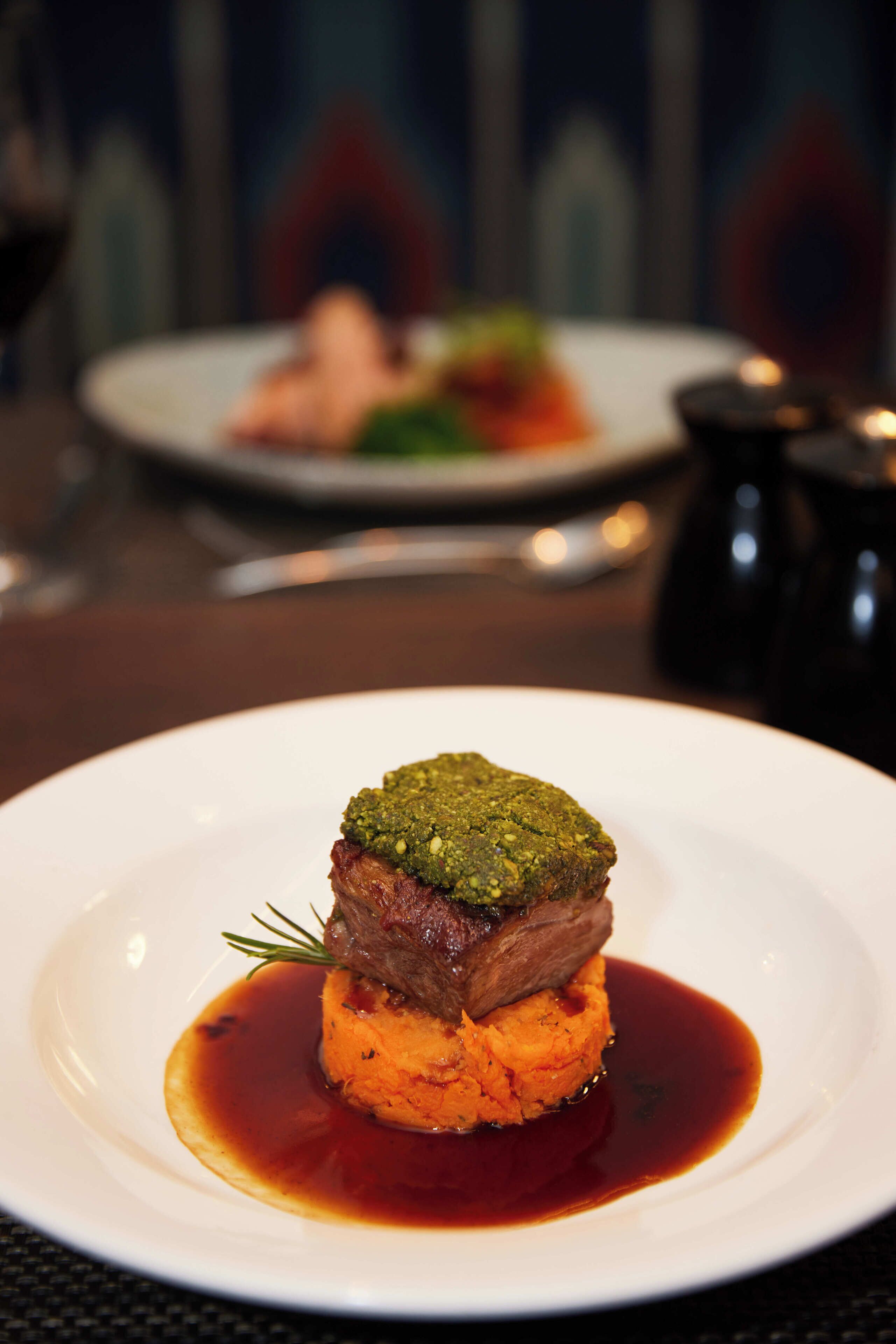 A plate with a meat dish on a bed of mashed potatoes, accompanied by a sauce.