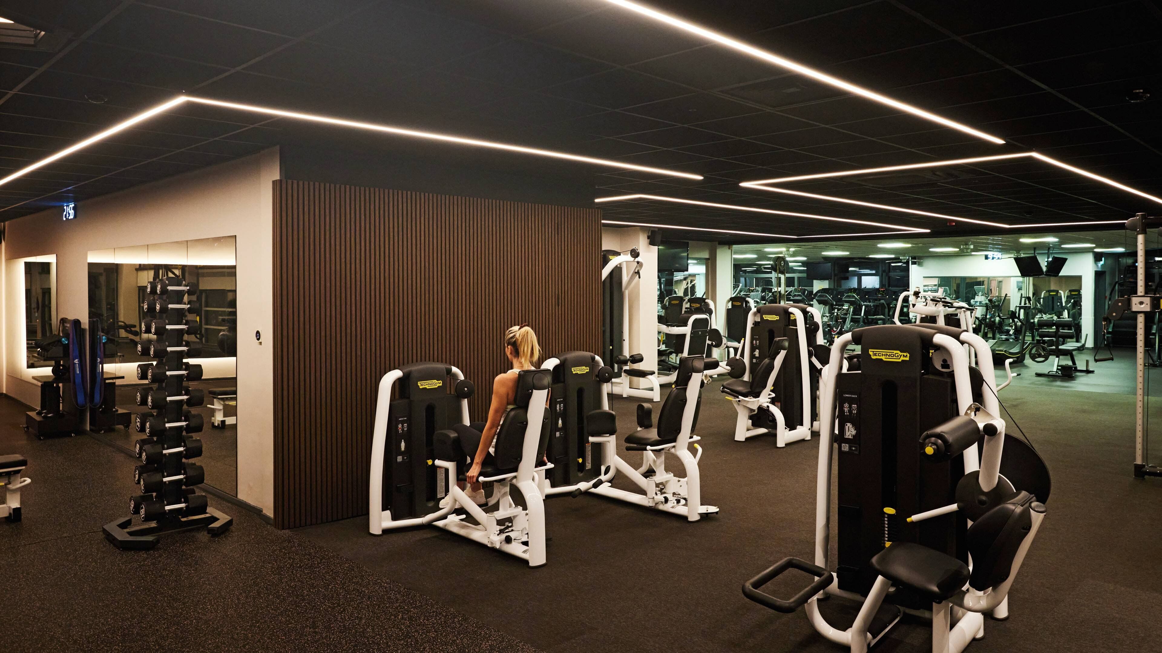 Un gimnasio con diferentes máquinas de ejercicio, un soporte para pesas y un espejo.