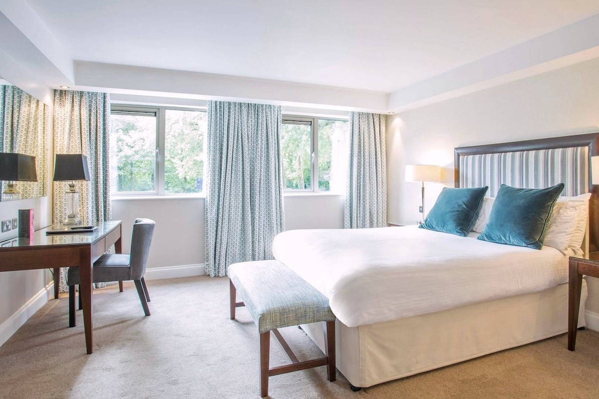 A hotel room with a large bed, a desk, a chair, and a window with curtains.