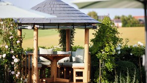 A wooden gazebo with a table and chairs, surrounded by lush greenery and flowers. - The Wrightington Hotel & Health Club (Wigan)
