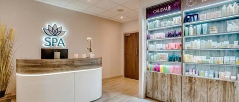 A spa reception area with a wooden reception desk, a neon sign, and a wall of spa products.