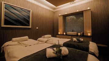 Relax in a serene spa room with two massage tables, a soothing painting, and warm ambient lighting.