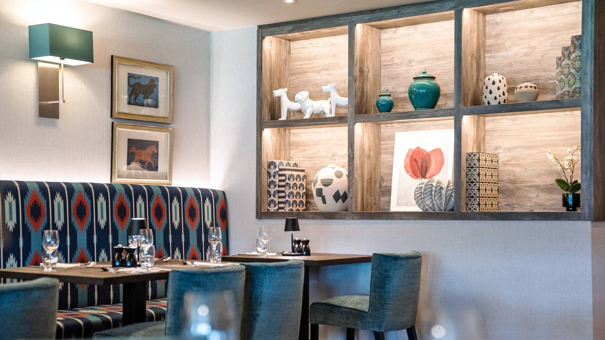 A modern dining area with a wooden bench, tables, chairs, and a wall display of decorative items.
