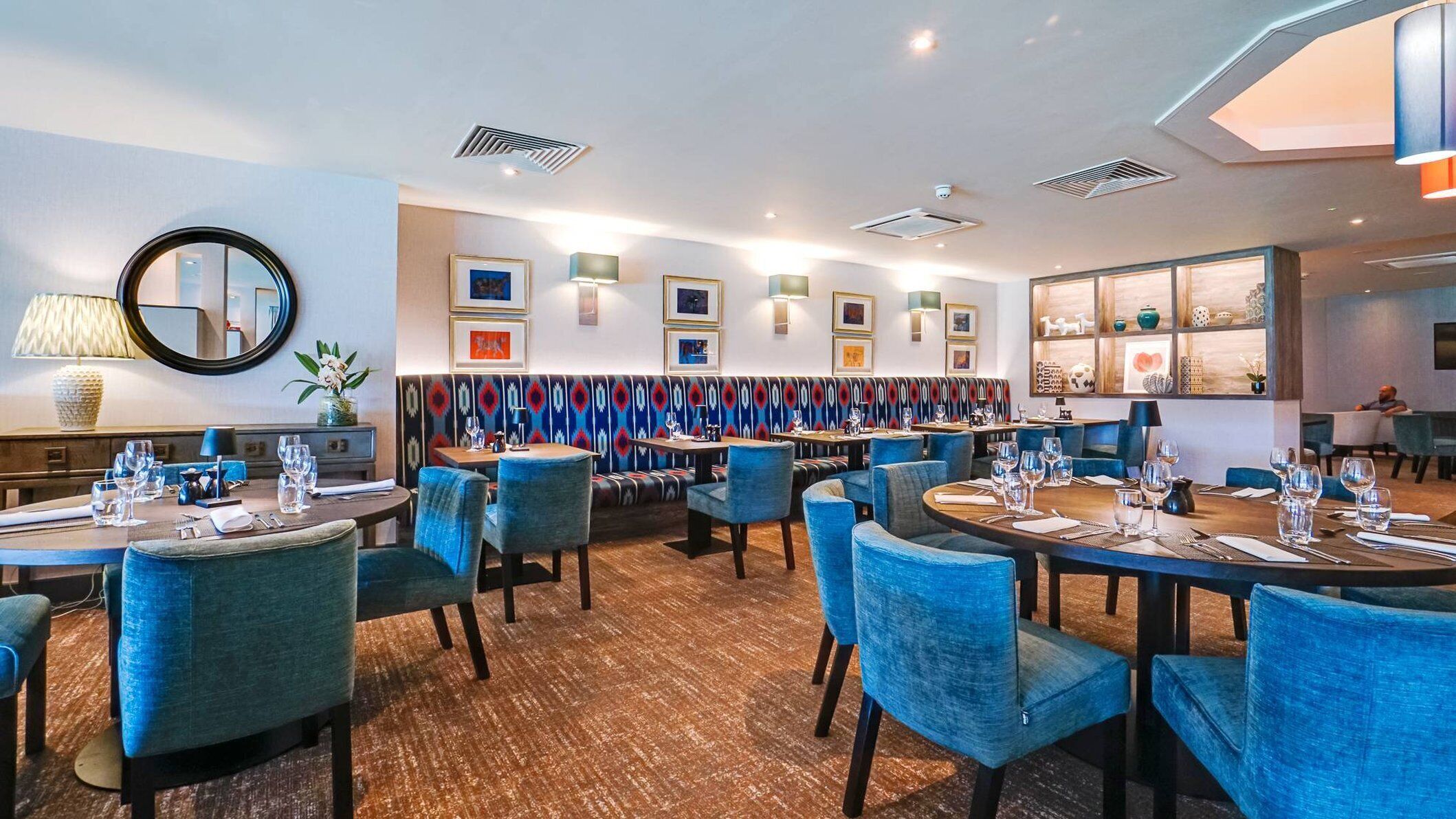 Een restaurant met ronde tafels, blauwe gestoffeerde stoelen en een behang met patroon.