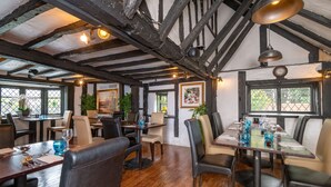 A restaurant with exposed wooden beams, large windows, and a mix of leather and fabric seating. - Donnington Manor Hotel (Sevenoaks)