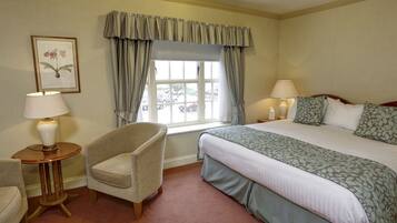 A hotel room with a large bed, two bedside lamps, a chair, a small table, and a window with curtains.