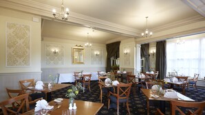 Una sala da pranzo formale con diversi tavoli apparecchiati, eleganti lampadari e carta da parati decorata.