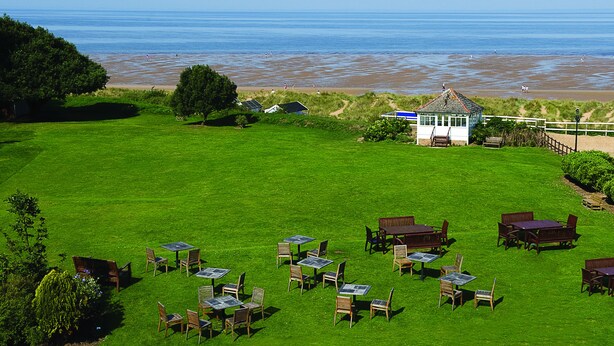 Un'area verde all'aperto con tavoli e sedie, un gazebo e vista sulla spiaggia e sull'oceano.