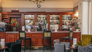 A bar area with wooden cabinets, multiple liquor bottles, and bar stools. - Moore Place Hotel, BW Signature Collection (Milton Keynes)
