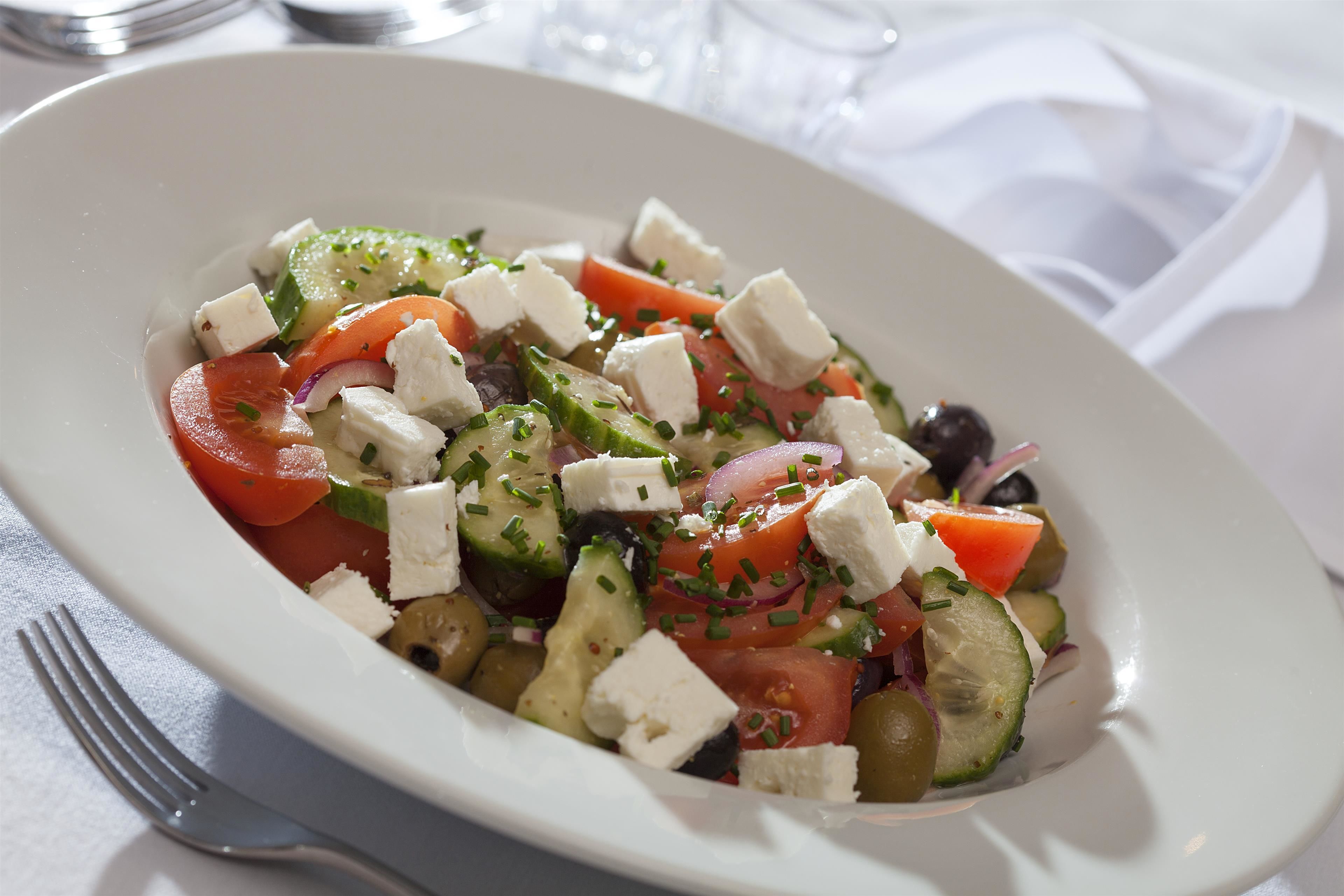 A white plate with a salad containing tomatoes, cucumbers, olives, and feta cheese.