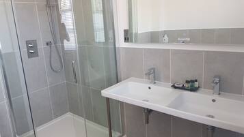 Un baño moderno con ducha envuelta en vidrio, un lavabo blanco con espejo arriba y azulejos grises.