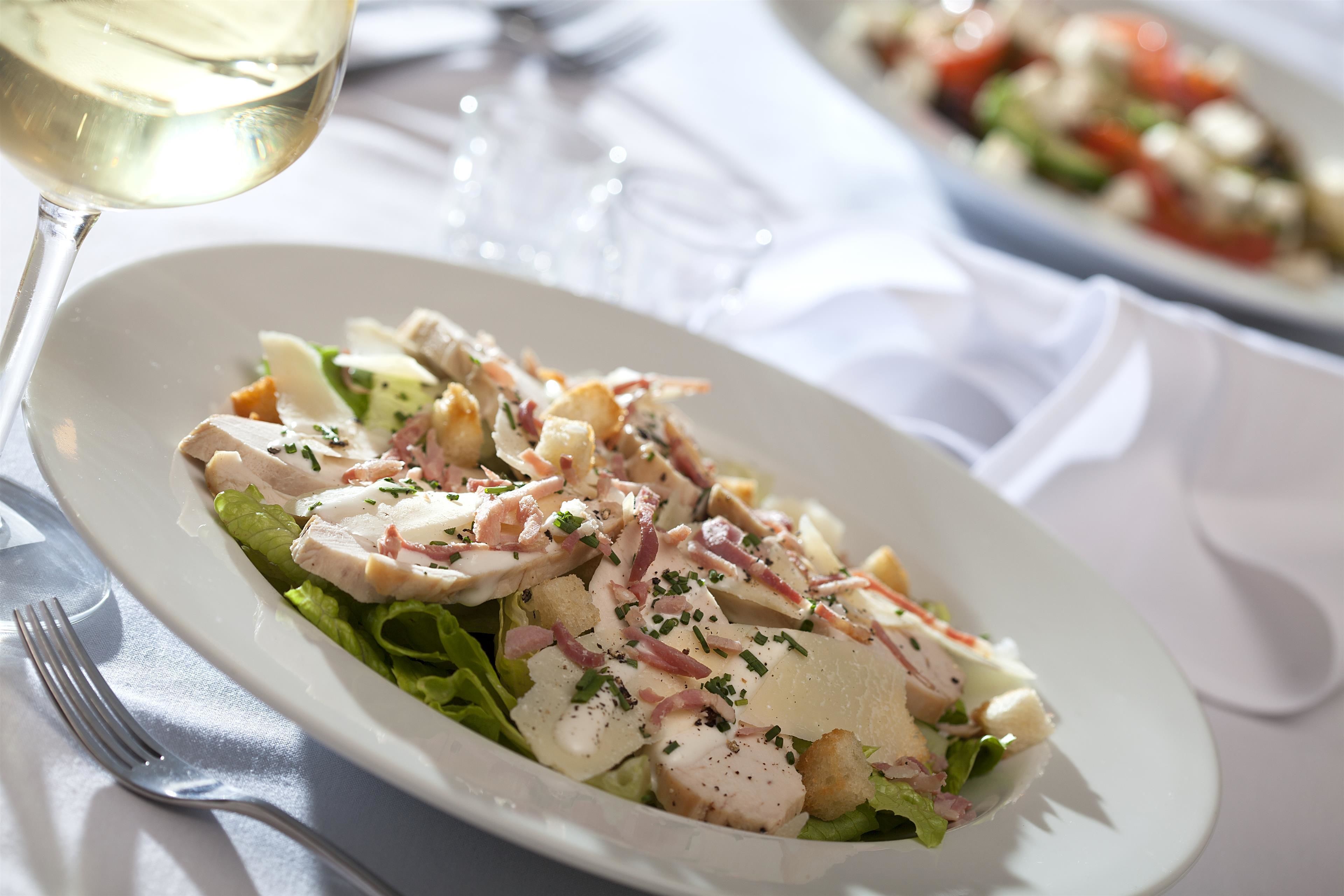 A plate of food with a fork and a glass of white wine on a table.