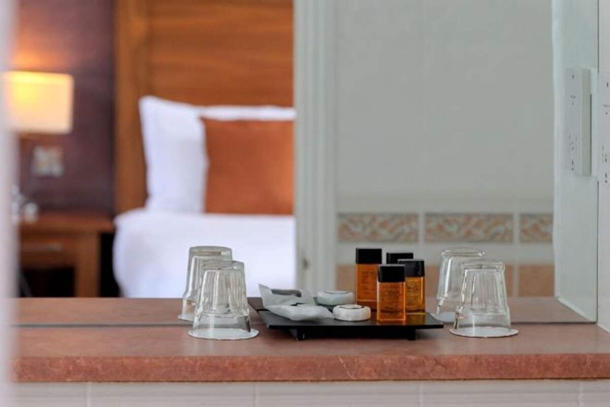 A hotel room with a bed, a nightstand, a tray with glasses and condiments, and a bathroom door.