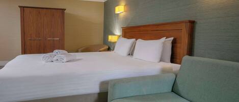 A hotel room with a large bed, a wooden wardrobe, a green armchair, and two bedside lamps.