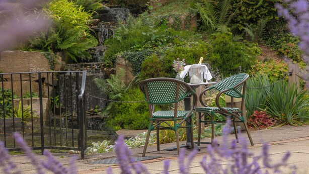 A patio with two green chairs and a table, surrounded by lush greenery and a small waterfall. - Moore Place Hotel, BW Signature Collection (Milton Keynes)