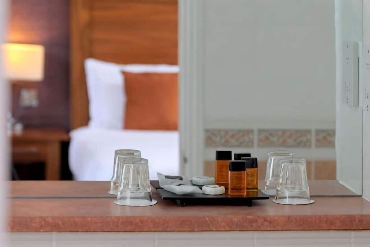 A hotel room with a bed, a nightstand, a tray with glasses and condiments, and a bathroom door.
