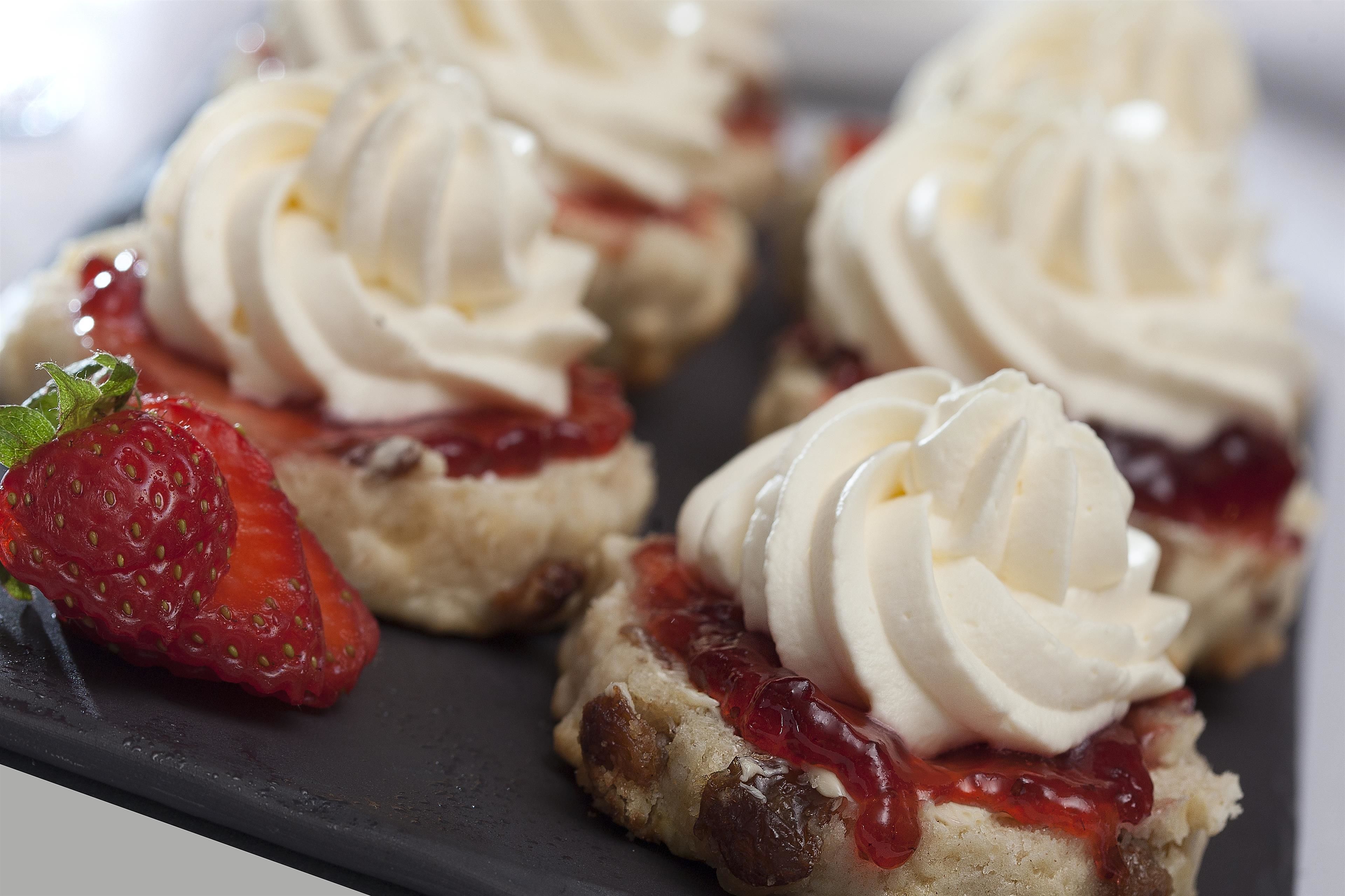 A dessert plate with scones topped with whipped cream and strawberry jam.