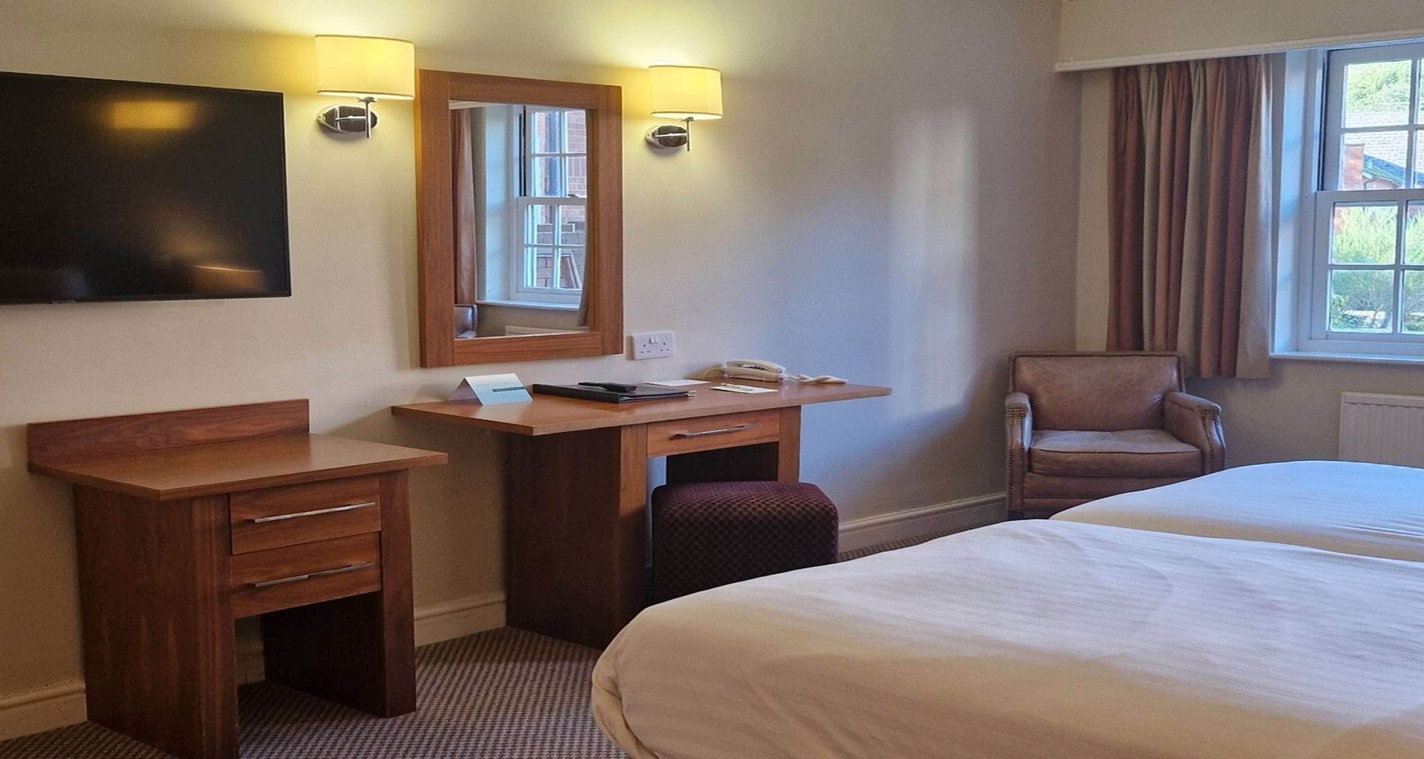 Habitación de hotel con cama, escritorio con silla, televisor y ventana con cortinas.