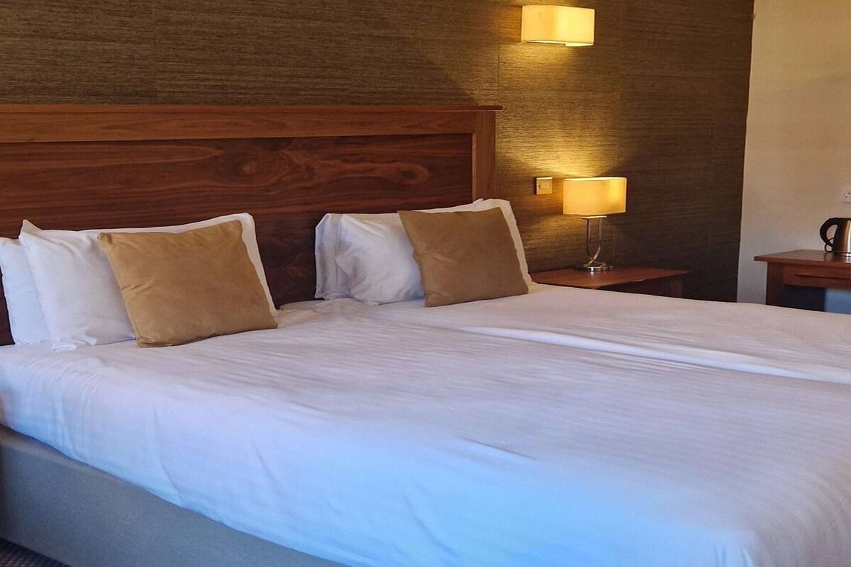 A neatly made bed with white and brown pillows, a wooden headboard, and a bedside lamp.