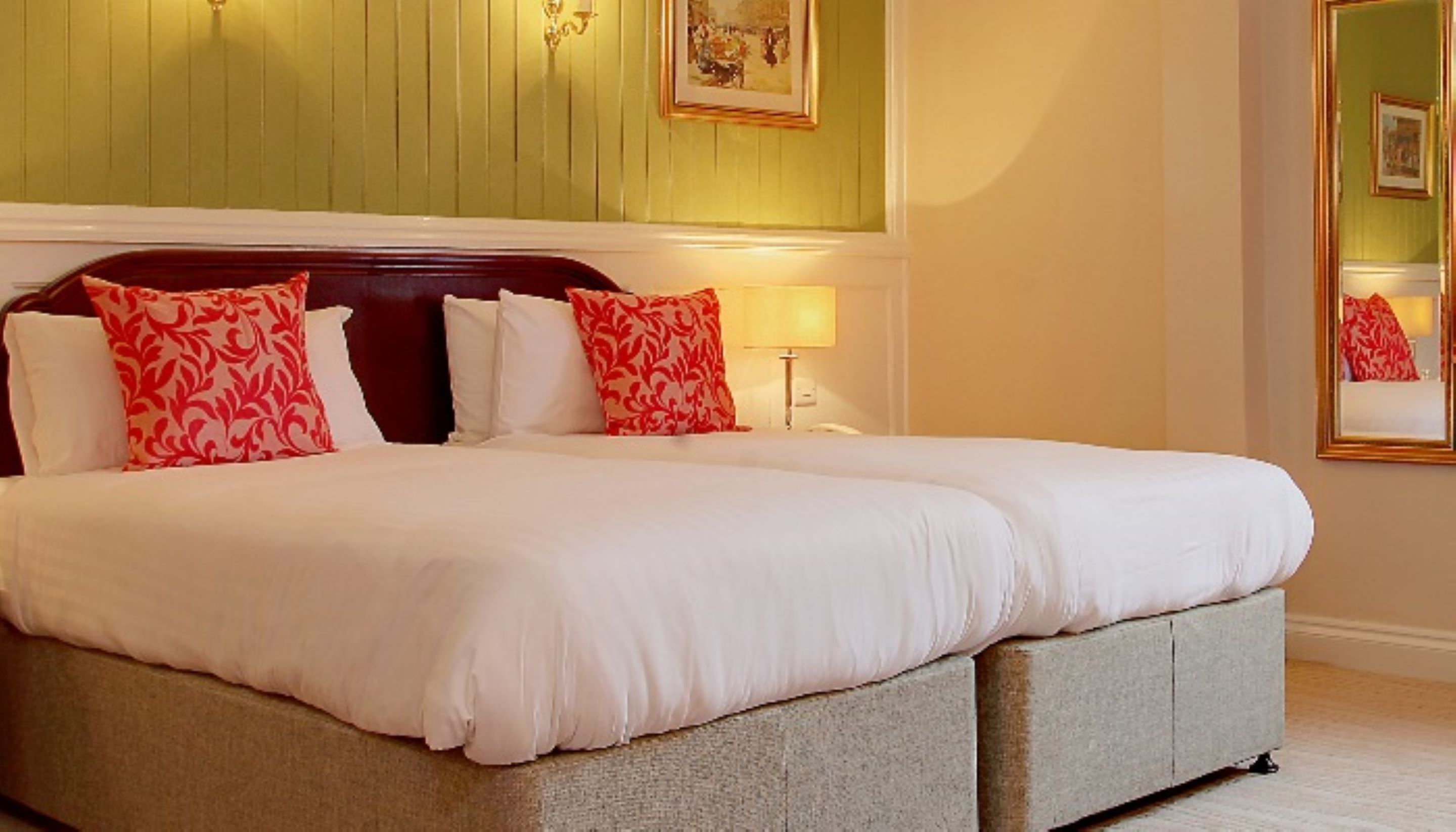 A large bed with white and red patterned pillows, a wooden headboard, and a bedside lamp.