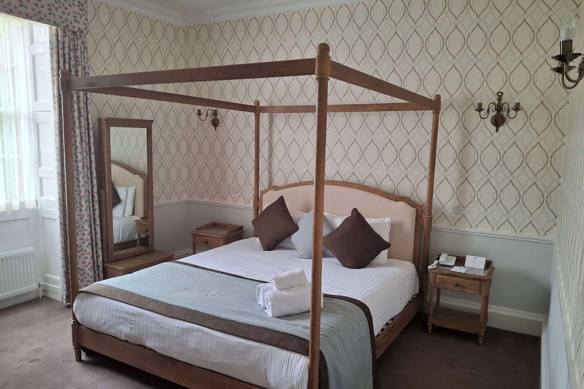 A four-poster bed with a mirror, two bedside tables, and a nightstand.