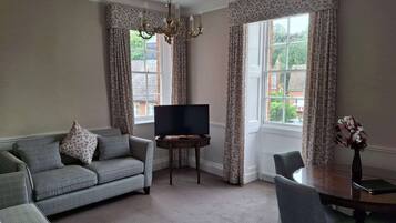 A living room with a sofa, a TV, a dining table, and a chandelier.