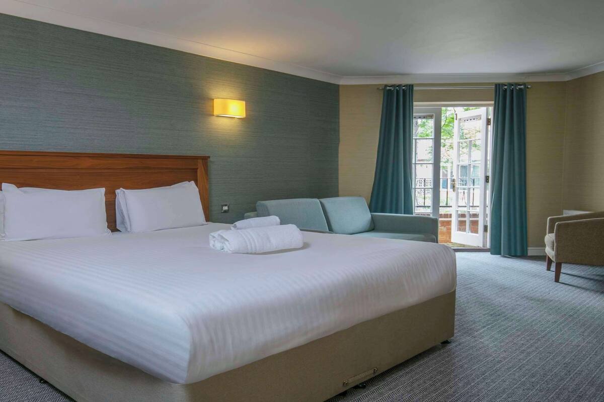 A hotel room with a large bed, a desk, a chair, and a view of the outdoors.