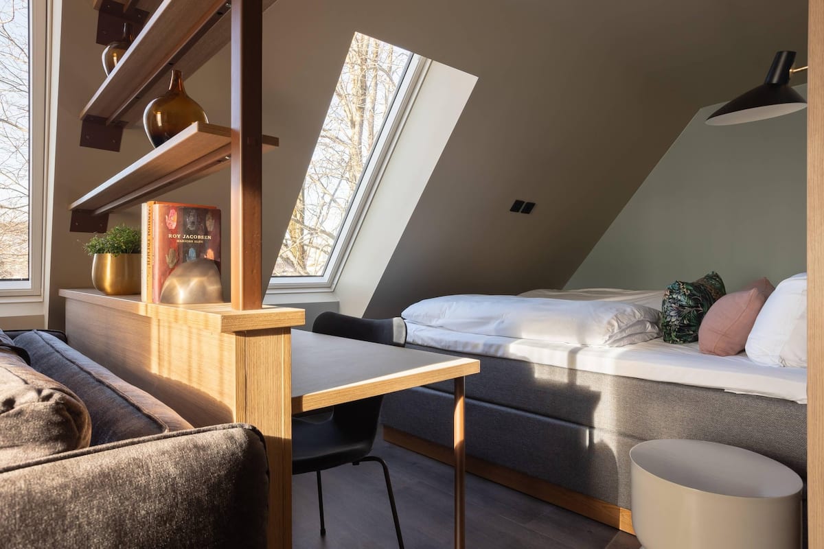 Ein modernes Schlafzimmer im Loft-Stil mit Dachfenster, einem Bett, einem Schreibtisch und einer Couch.