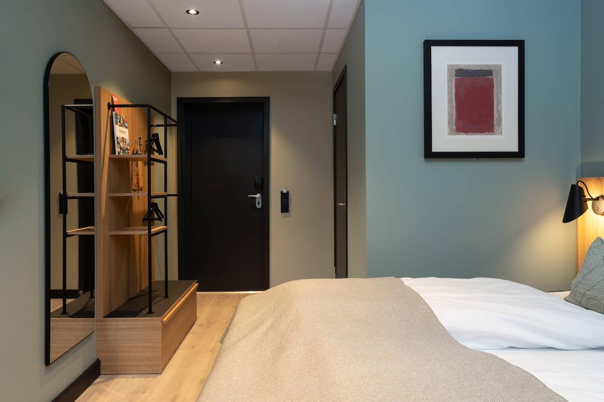 Ein Schlafzimmer mit Bett, Kleiderschrank, einer Tür und einem gerahmten Bild an der Wand.